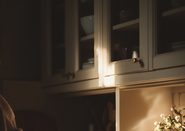 Frau greift abends im warmen Licht in den Küchenschrank – Symbolbild für Zucker als Belohnung nach einem anstrengenden Tag